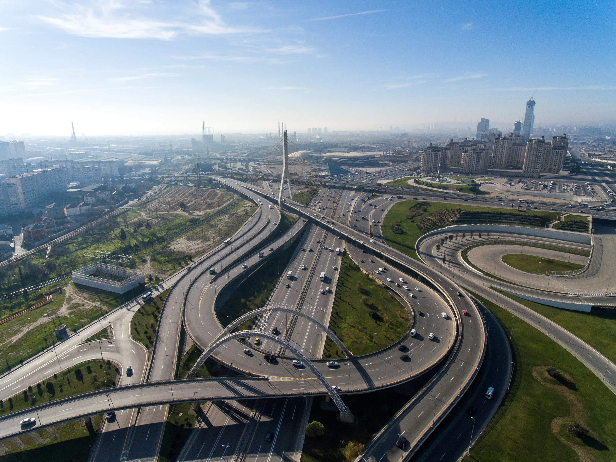 Aerial view of a multi-level highway interchange in a city with tall buildings in the background, under a clear blue sky.