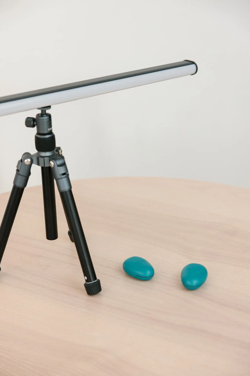 A camera on a tripod, a light bar, and two blue wireless earbuds on a wooden surface.