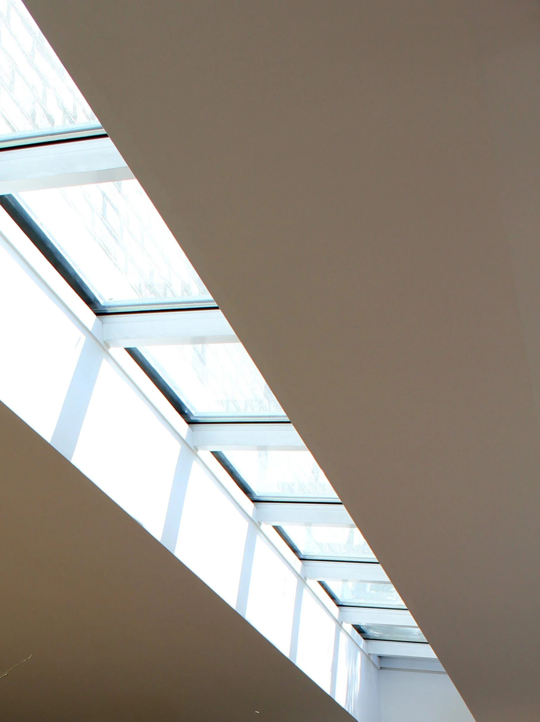 Interior view of a skylight window on the ceiling, allowing natural light into the room, with a part of a brown ceiling visible.