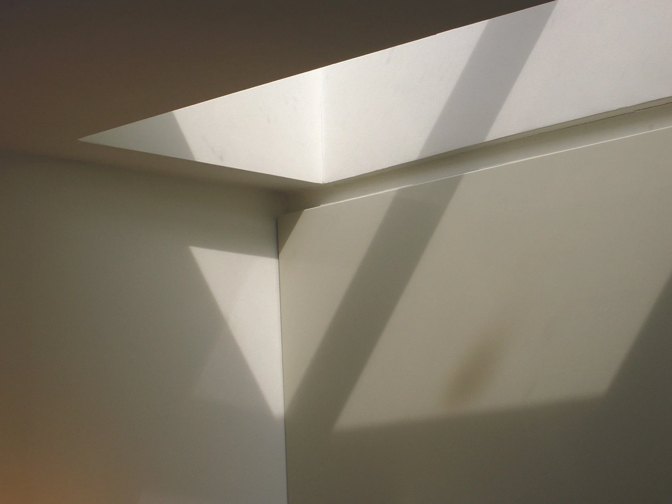 A white ceiling with a rectangular light fixture casting shadows on the ceiling and wall.