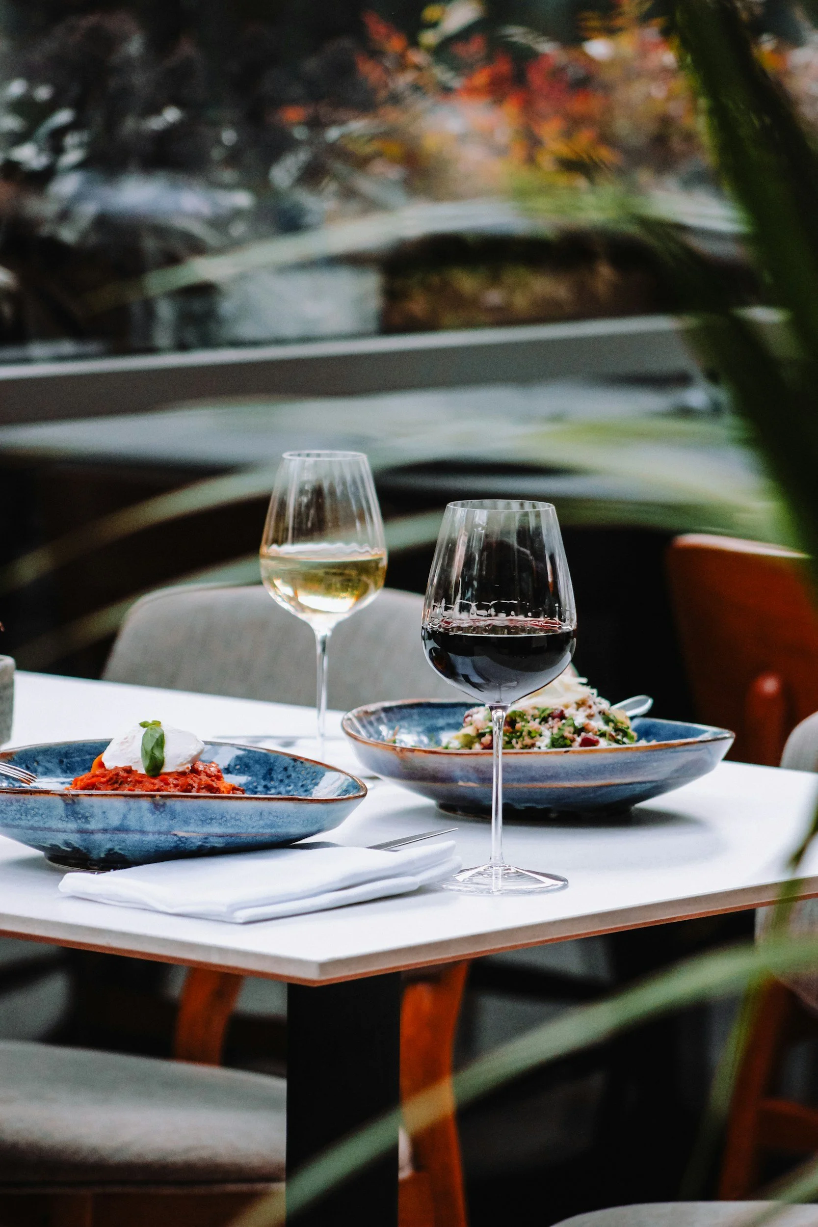 Mesa con platos de comida y copas de vino en un restaurante, con fondo de plantas verdes y ambiente elegante.