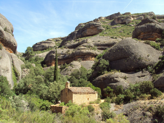 Pequeña iglesia de piedra en un paisaje montañoso con rocas y vegetación.