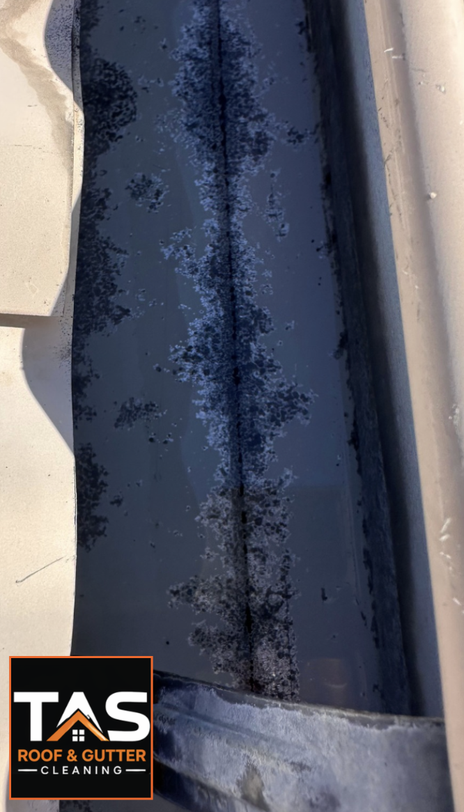 Interior of a metal roof gutter after larger debris removal, showing remaining dark sediment marks and the importance of thorough internal gutter cleaning.