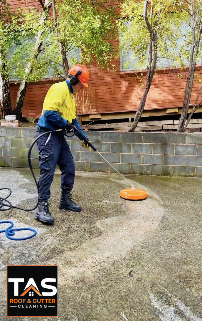 specialist using a rotary surface cleaner on stained concrete beside a retaining wall in Hobart.