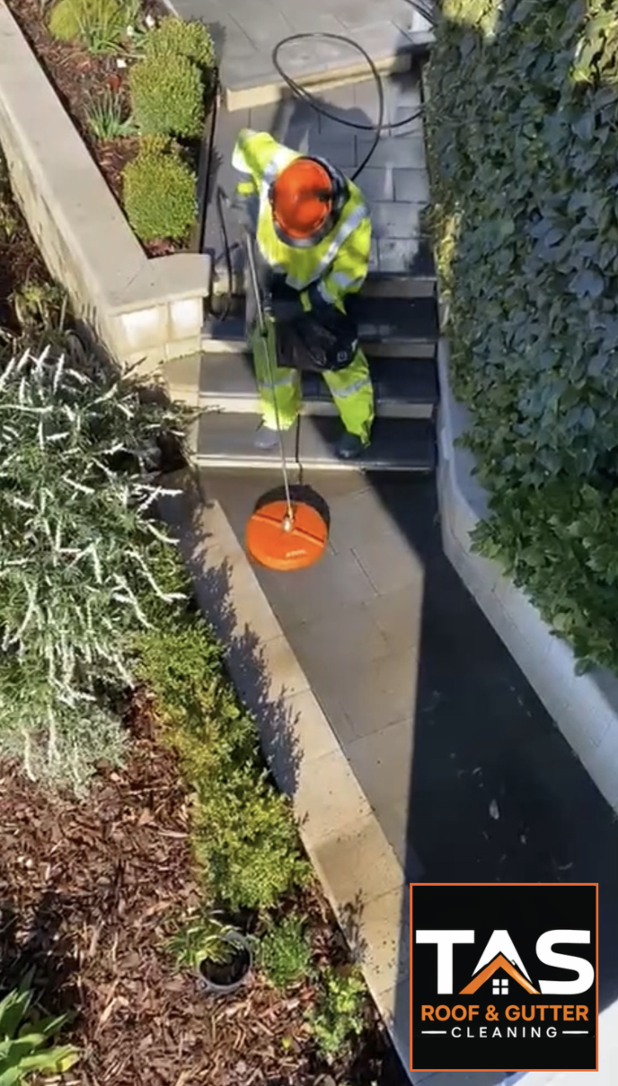 Technician pressure cleaning a paved garden path beside outdoor steps in Hobart.