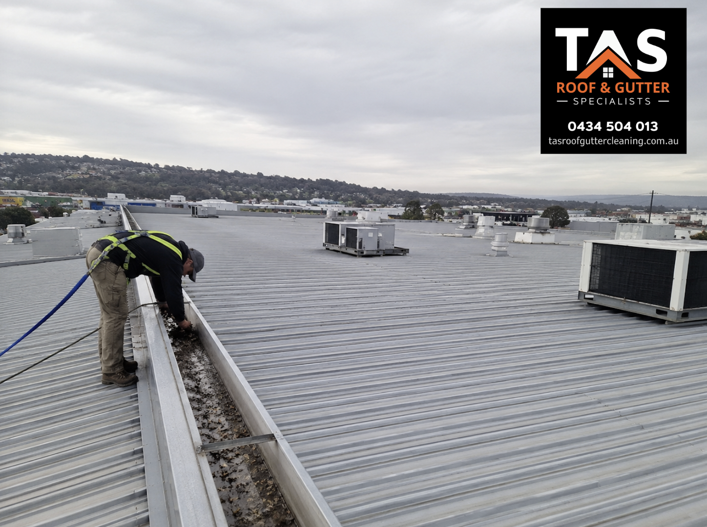 Commercial roof gutter cleaning in Burnie with technician clearing debris from a large metal roof gutter