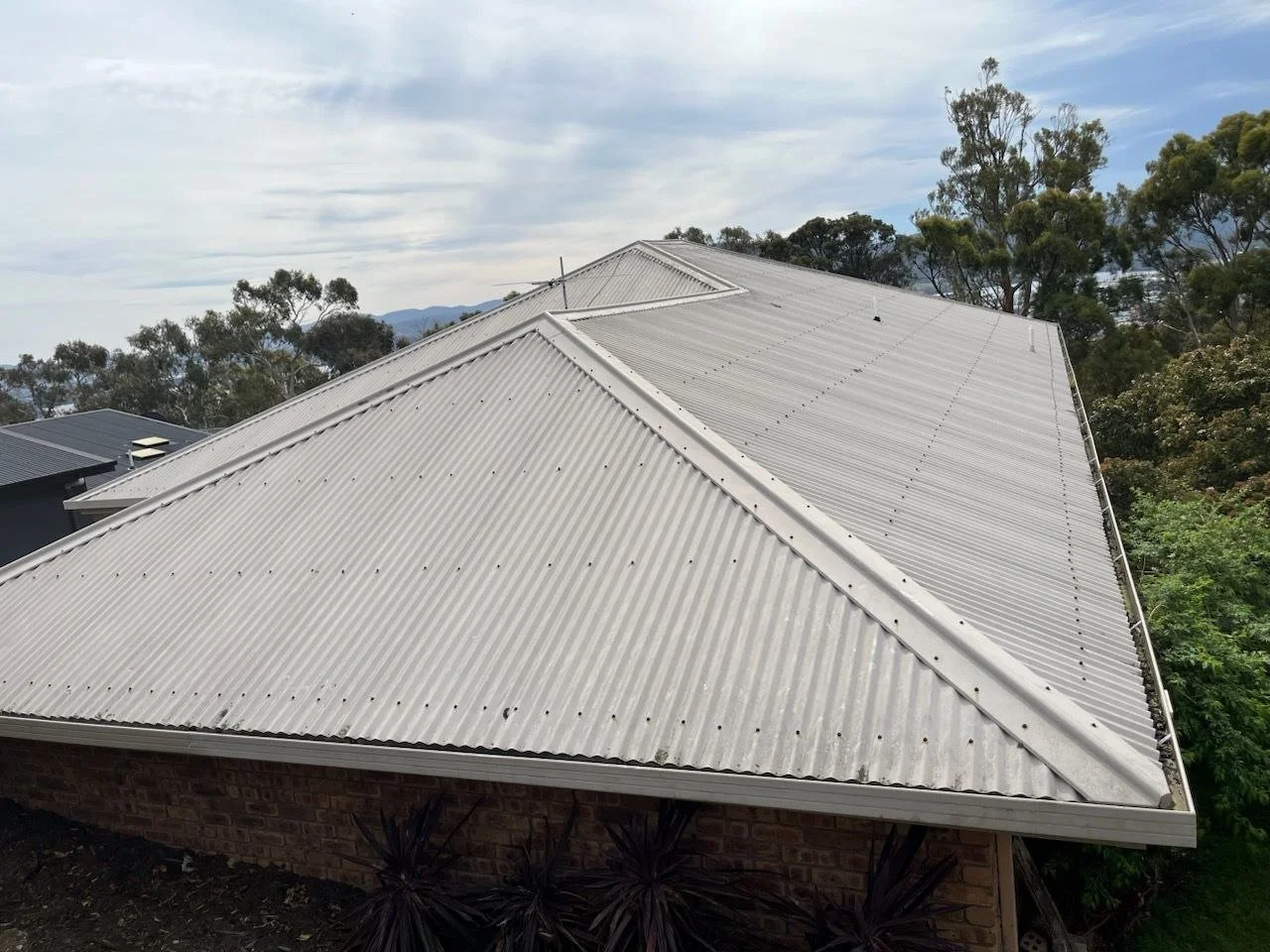 Corrugated metal roof and gutters on a brick house in West Moonah, Hobart, surrounded by established trees.