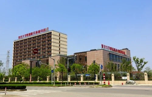 Large hospital building with Chinese signage, trees, street signs, and clear blue sky.
