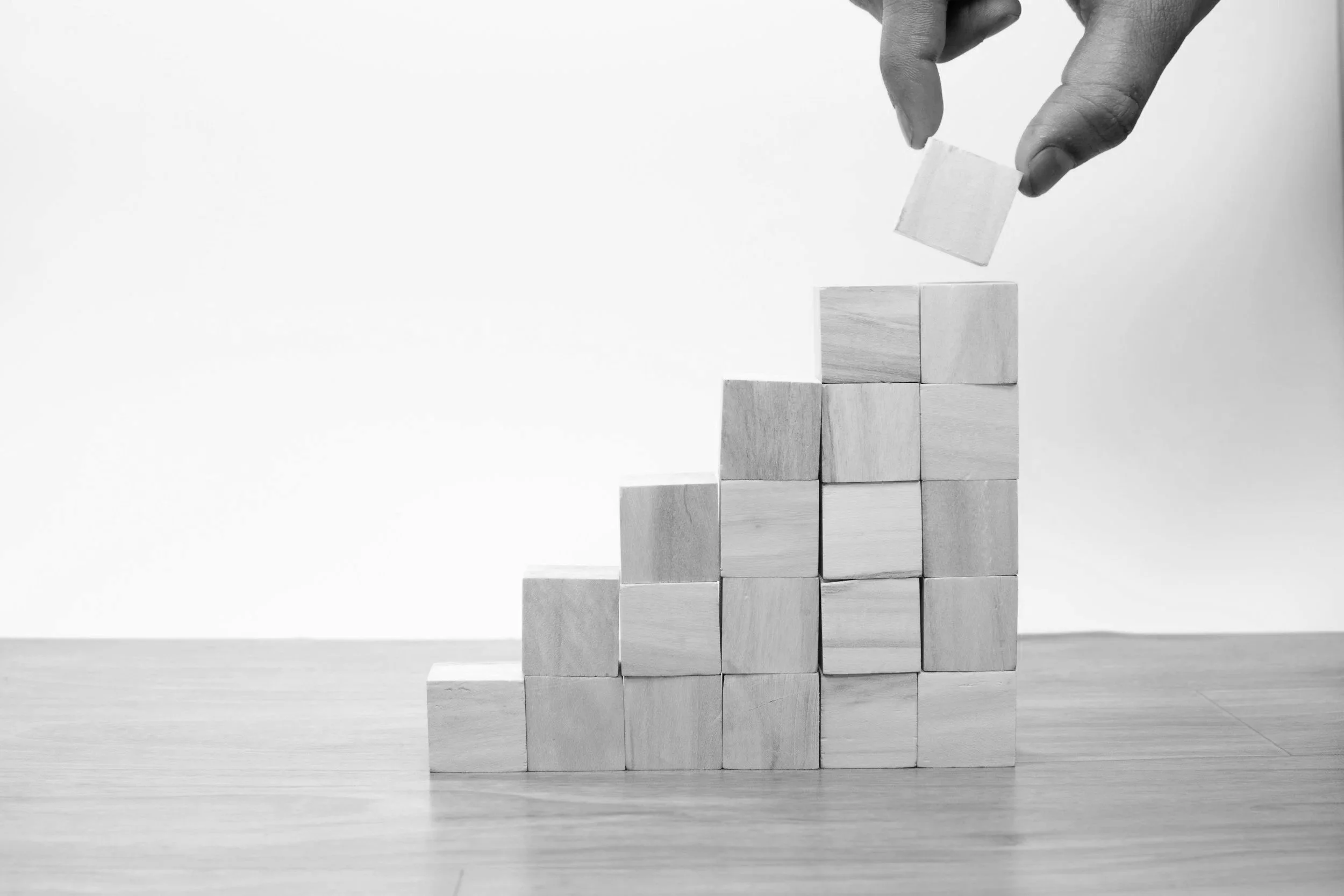 A hand placing a wooden block to build a tower of blocks.