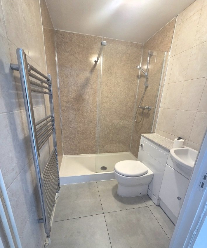 Repaired bathroom floor finished with large grey tiles beside the shower and toilet