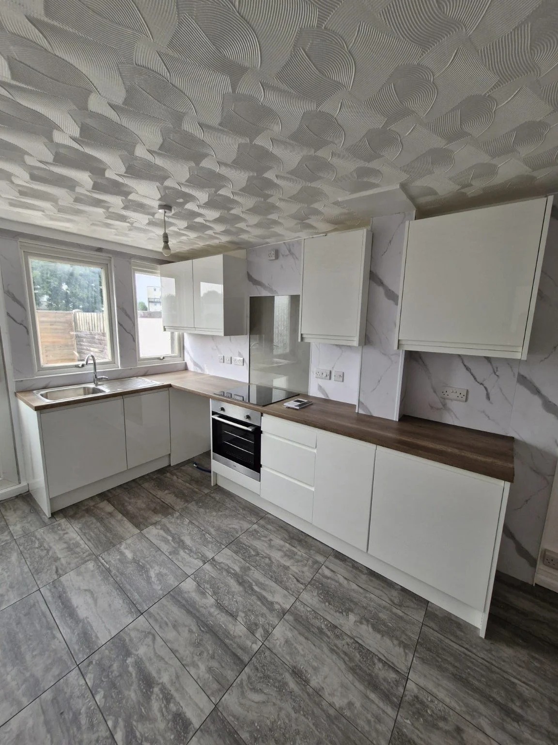 Refurbished Gosport rental kitchen with white cabinets, wood-effect worktops and grey floor tiles