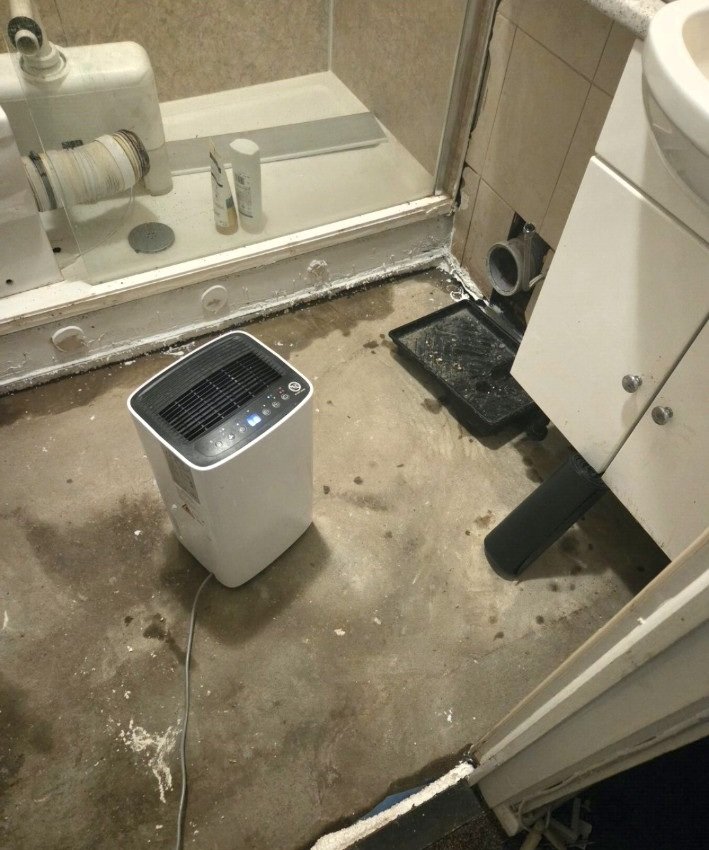 Exposed bathroom floor and dehumidifier during repairs following a leak