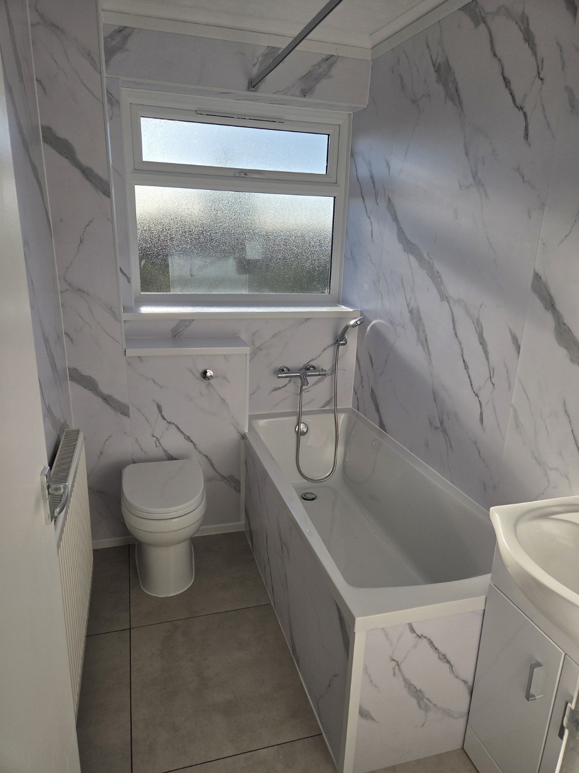 Refurbished Gosport rental bathroom with marble-effect walls, bath and grey tiled floor