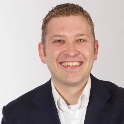 A smiling man in a dark suit and white shirt posing against a white background.