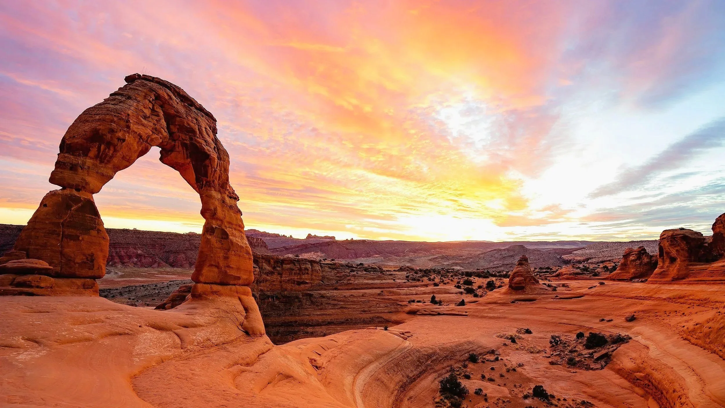A natural rock formation known as Delicate Arch during a colorful sunset in a desert landscape.