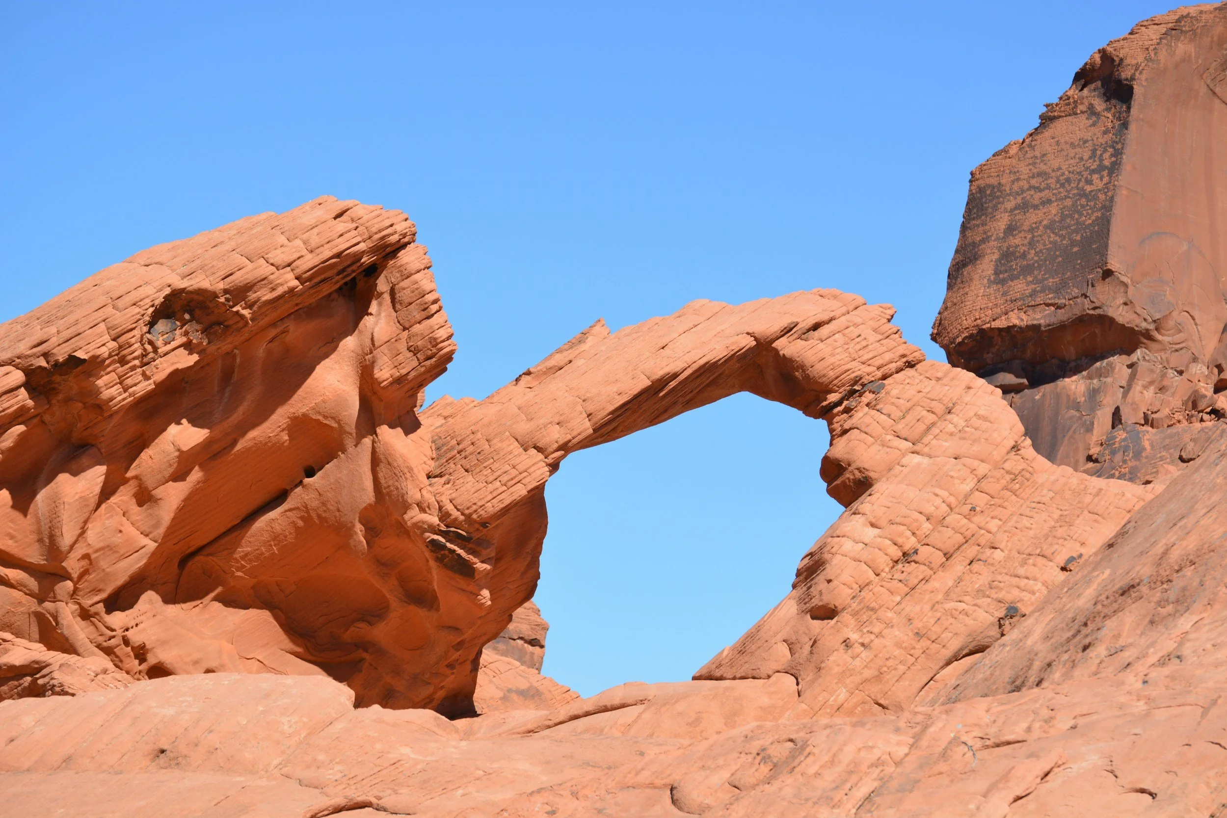 Red sandstone rock formations with a natural arch against a clear blue sky.