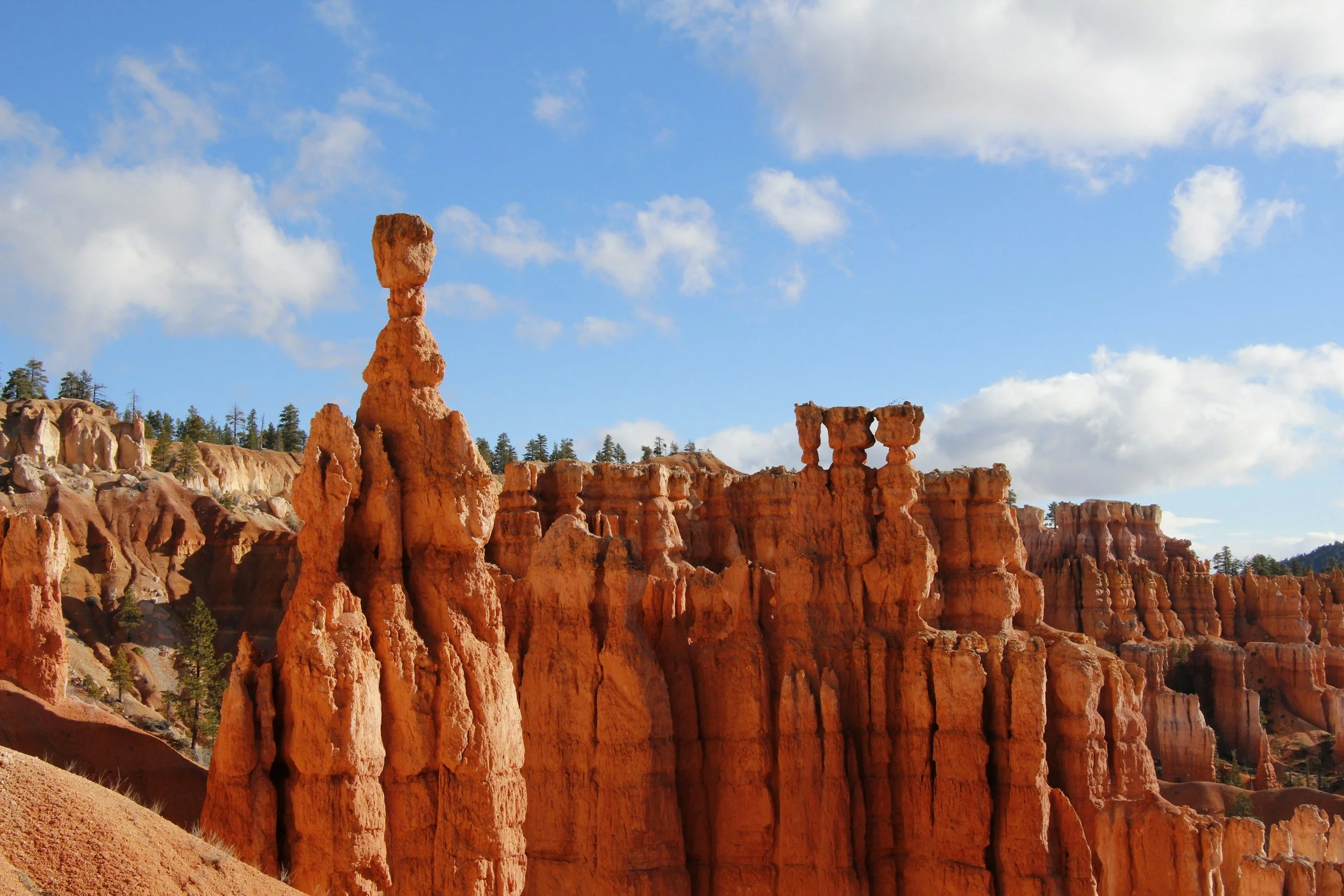 Red rock formations and hoodoos in Bryce Canyon National Park against a partly cloudy sky.