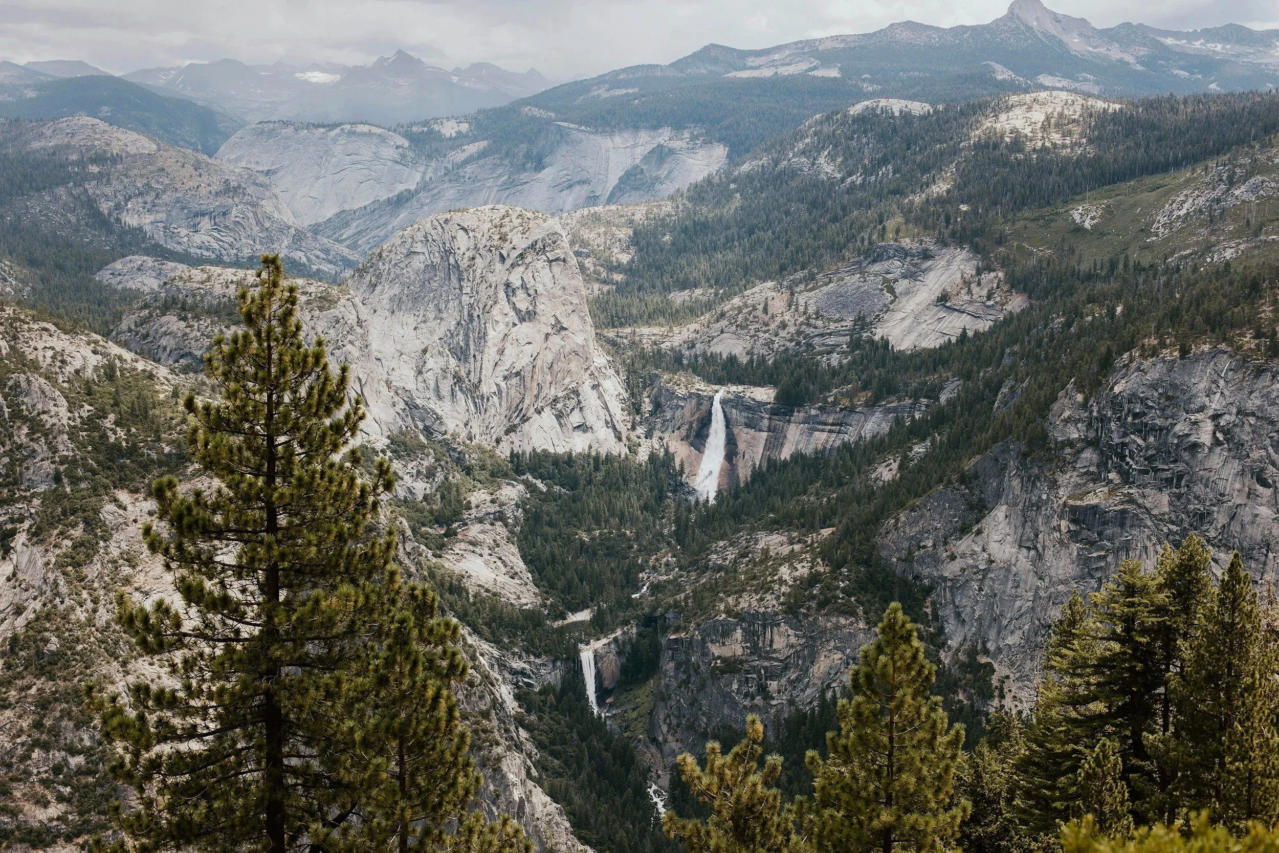A mountainous landscape featuring steep granite cliffs, lush green forests, and a waterfall in a remote wilderness area.