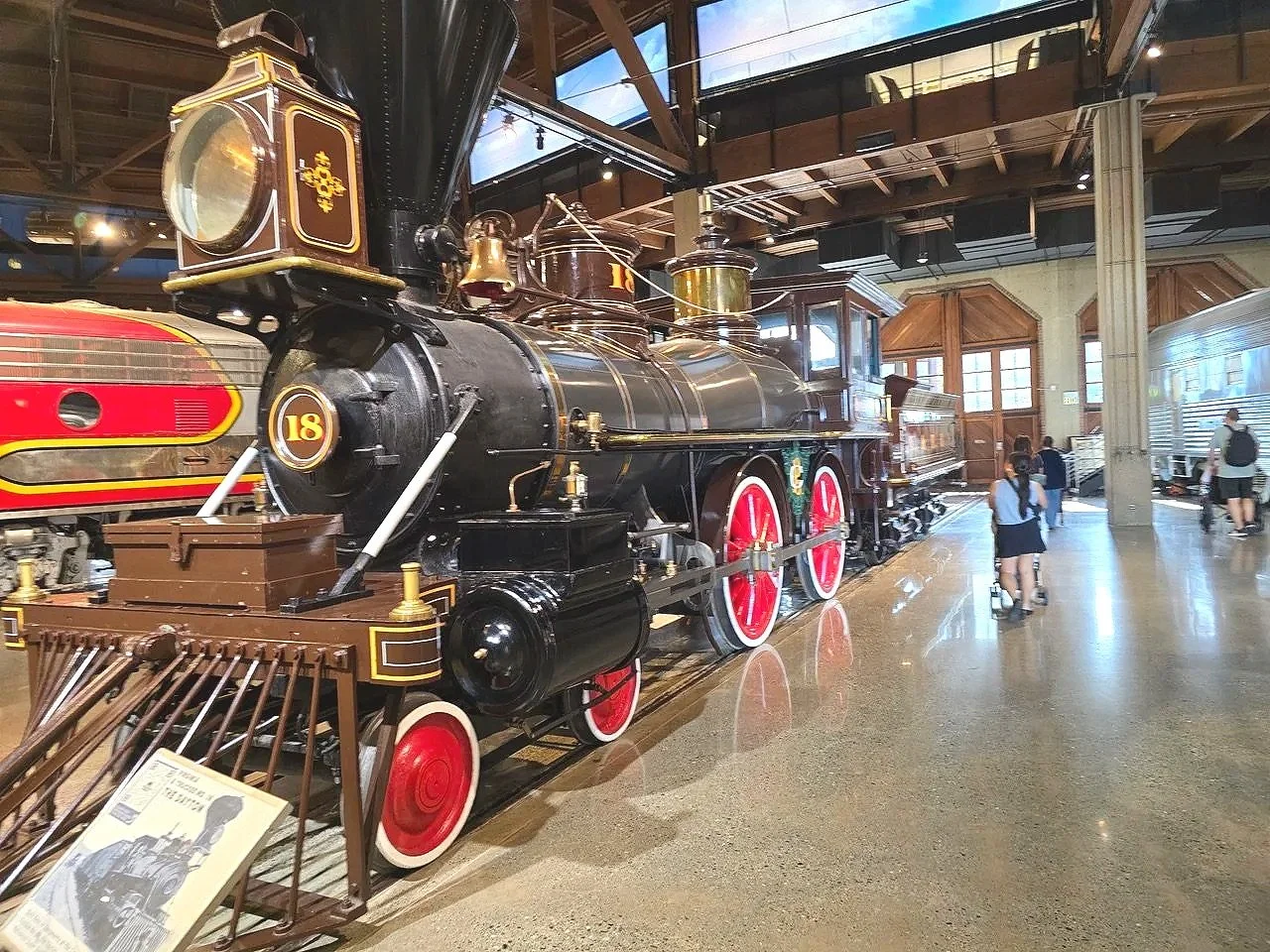 Vintage black steam locomotive with red and gold accents on display inside a museum, with visitors walking around.