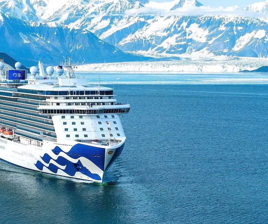 A large cruise ship sailing in icy waters with snow-covered mountains in the background.