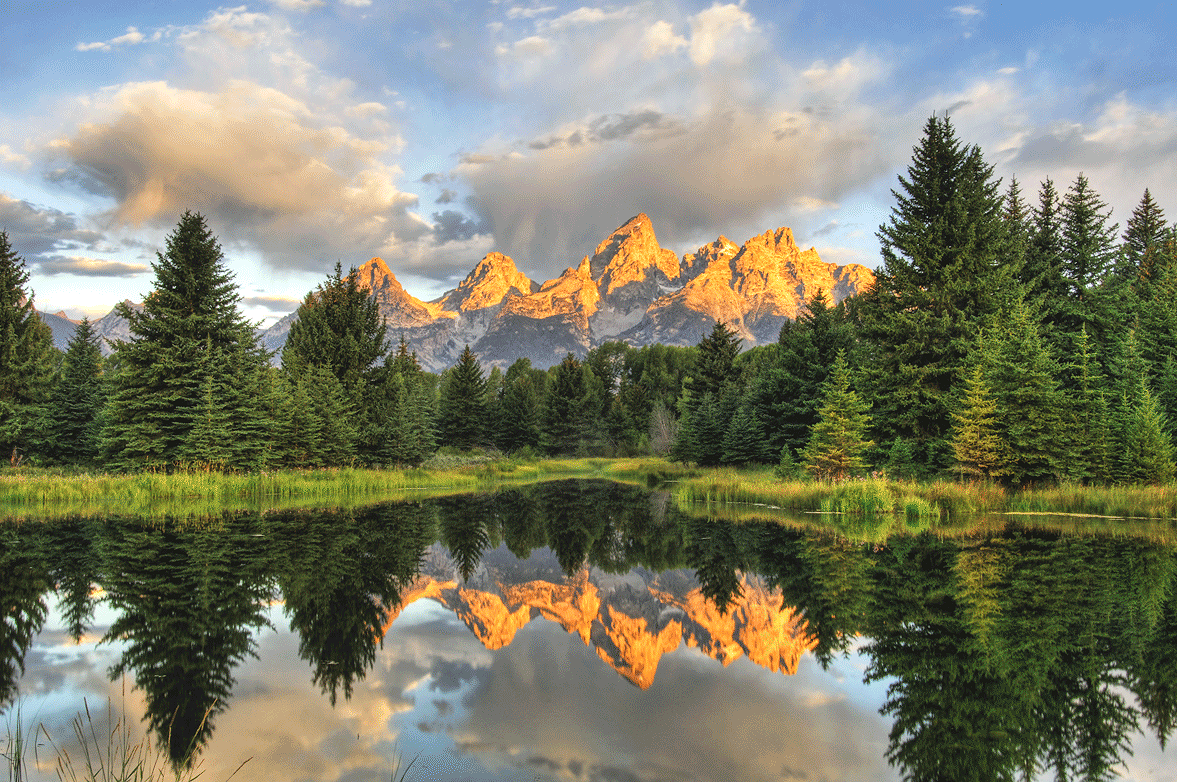 Mountains reflecting in a lake surrounded by trees at sunrise or sunset.