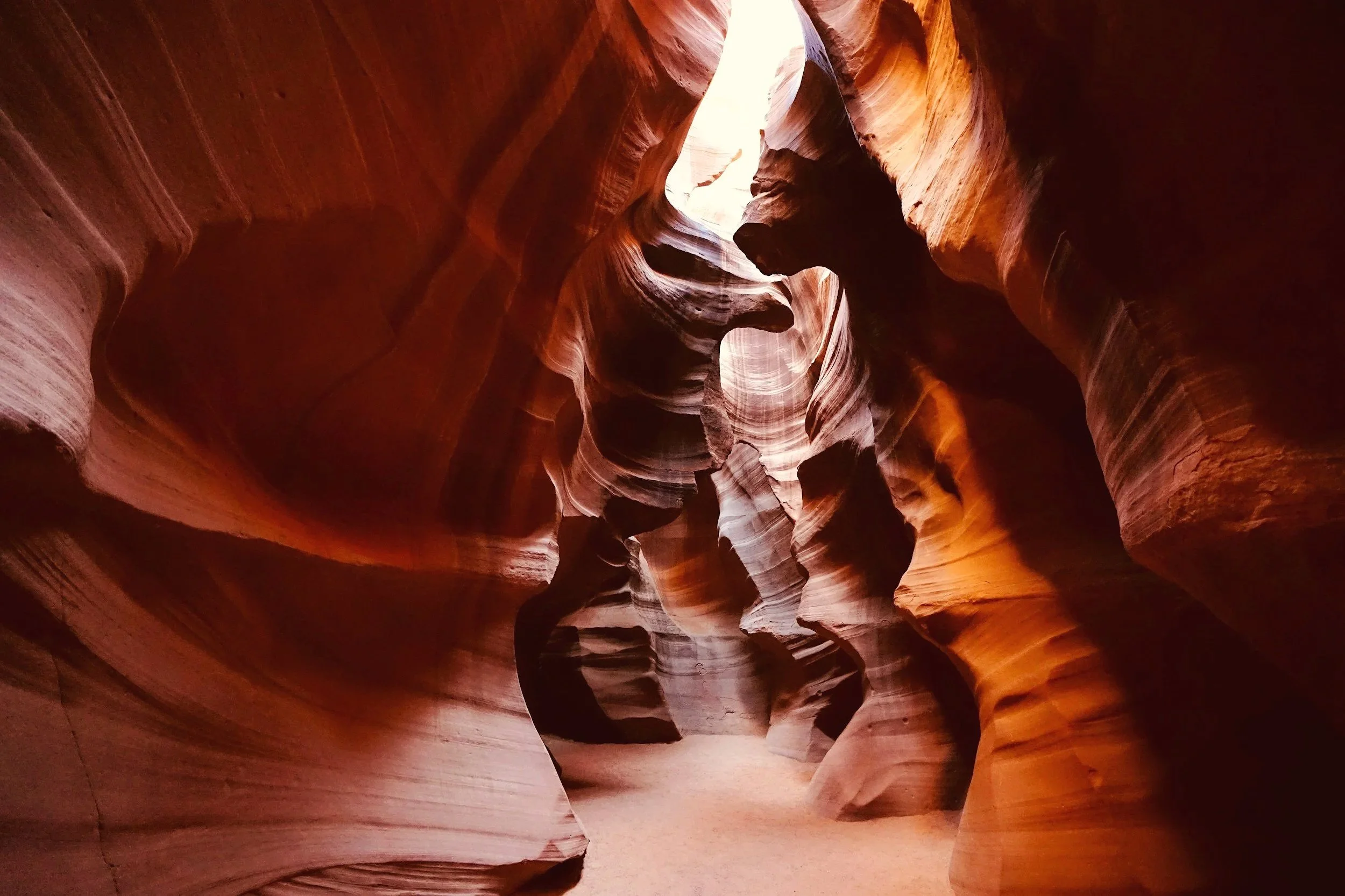 Inside Antelope Canyon showing smooth, layered sandstone walls in warm orange and reddish hues with a narrow opening at the top letting in light.