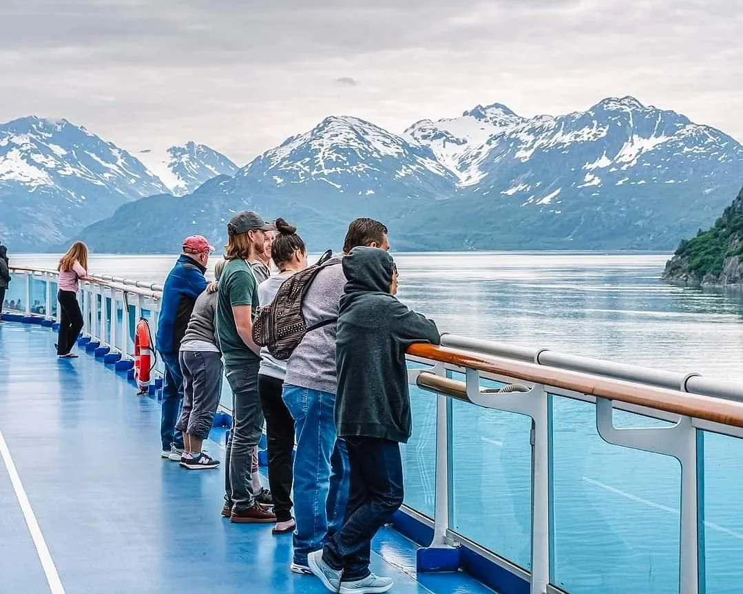 Tourists on a boat observing snow-capped mountains near a body of water.