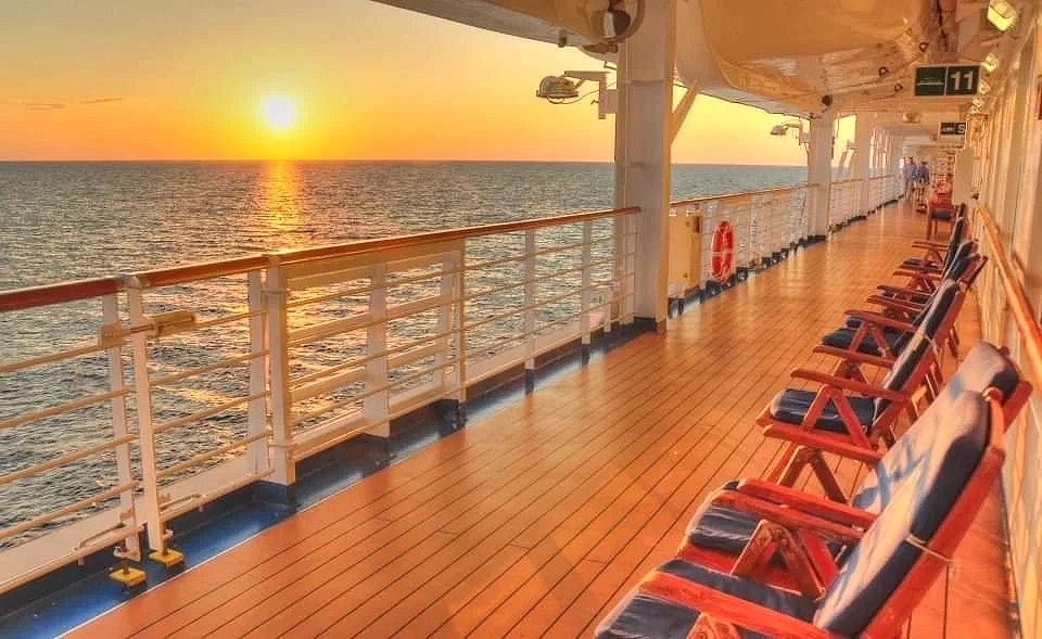 Sunset viewed from the deck of a cruise ship with empty chairs along the railing.