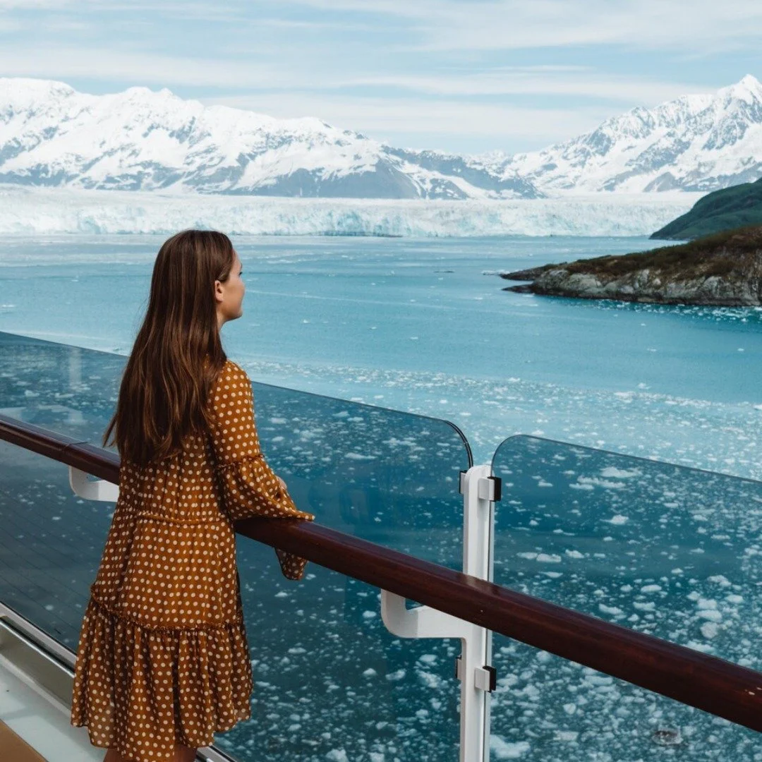 A woman with long brown hair looking out over icy water and snow-covered mountains from the deck of a cruise ship.