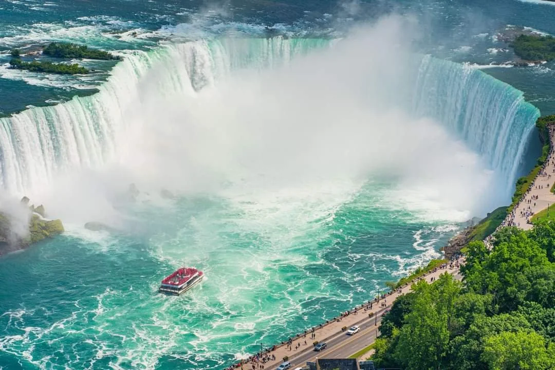 Niagara Falls with a boat on the river and visitors walking along the parkway.
