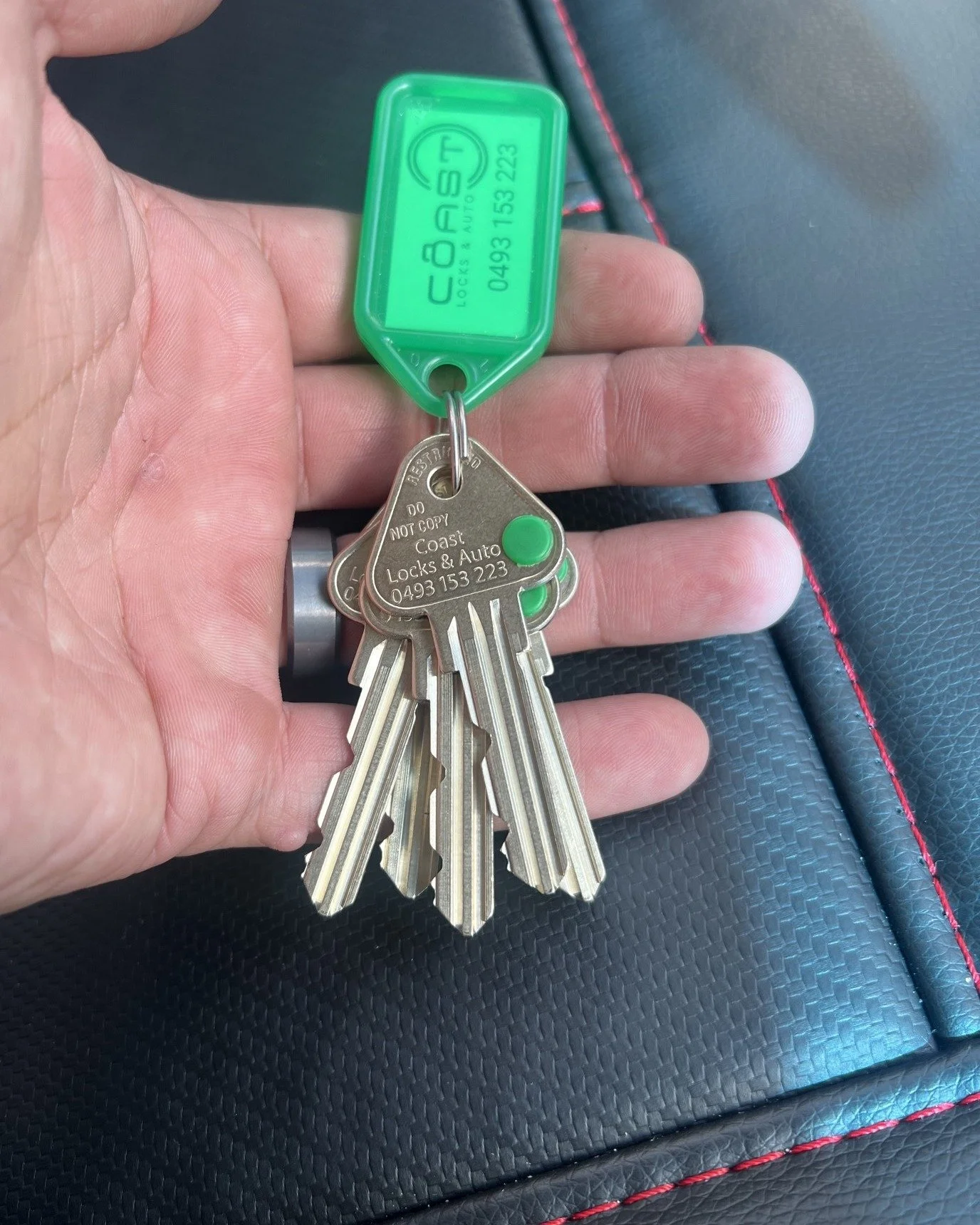Hand holding a set of car keys with a green key fob marked 'COAST Lock & Auto' and a transparent green plastic tag.