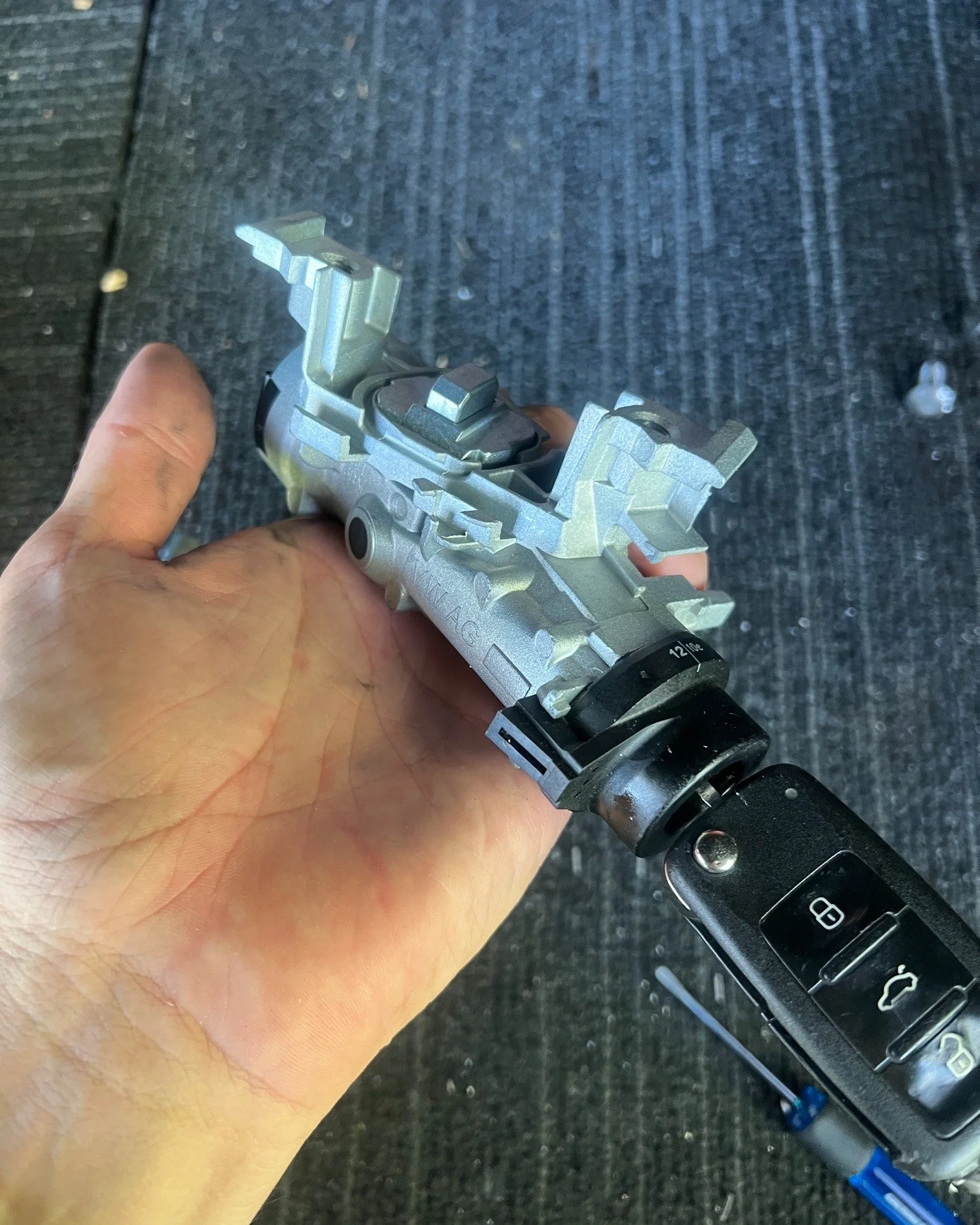Close-up of a person's hand holding a car key with the ignition lock cylinder exposed.