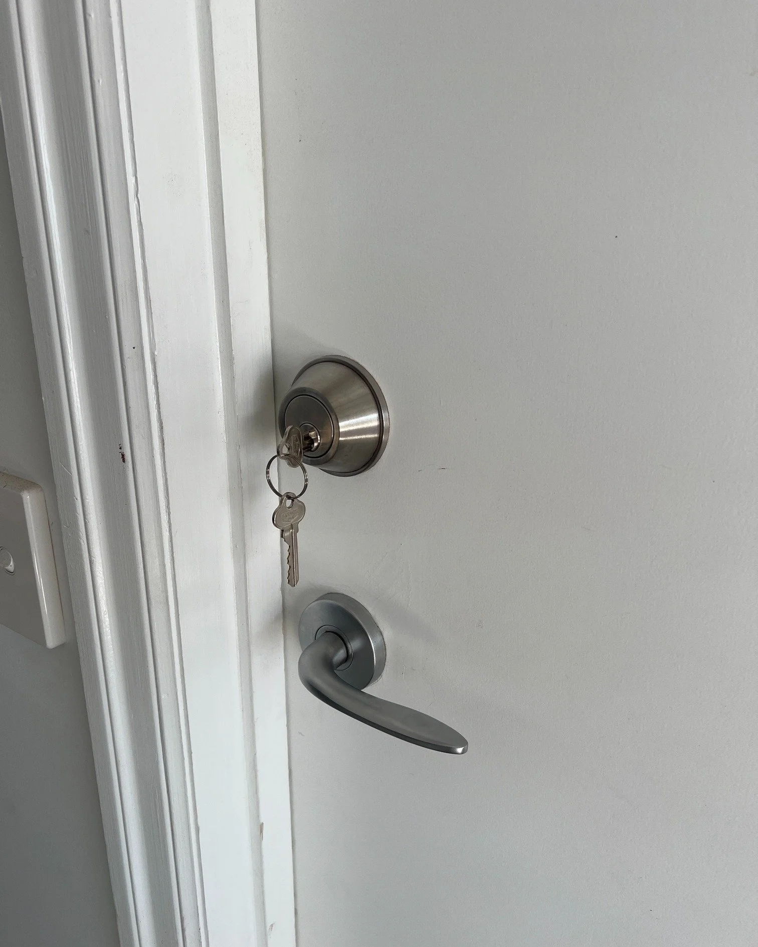 A white door with a metallic doorknob, a key inserted on a keyring, and a metallic lever handle.