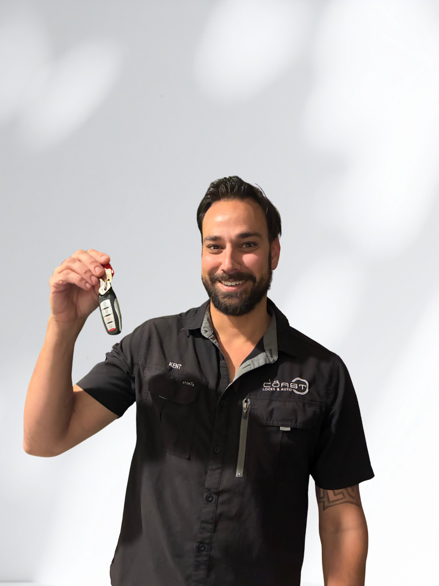 Smiling director Kent Fegan with dark hair and a beard holding a car key in front of a plain white background.