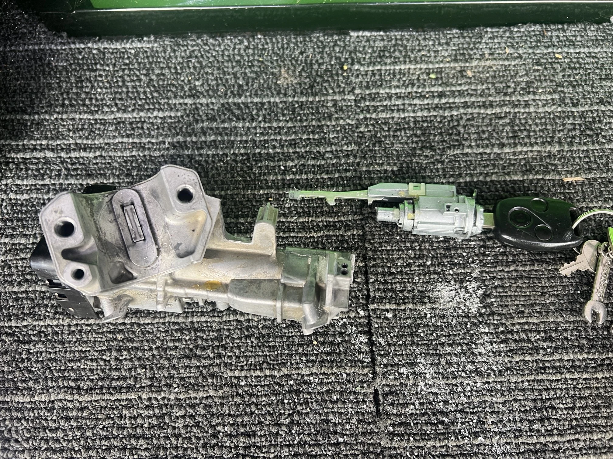 Automotive ignition switch assembly, including key fob, lying on a gray textured carpet.