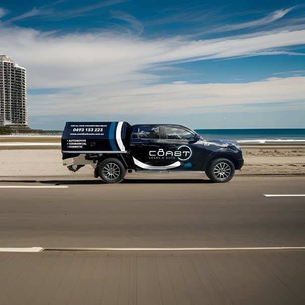 A black pickup truck with advertising for a locksmith service on the side, driving along a beachside road with the ocean and sky in the background.