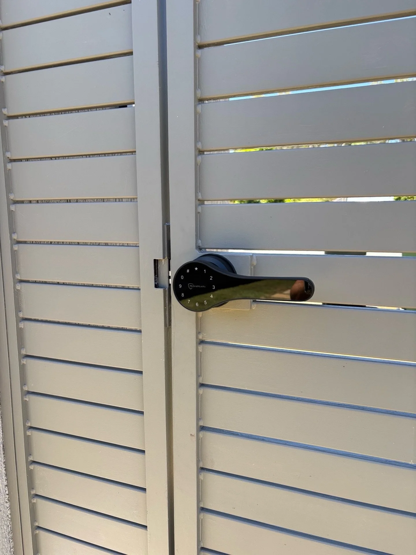 A silver-grey security door with horizontal slats, featuring a modern black digital door lock handle.