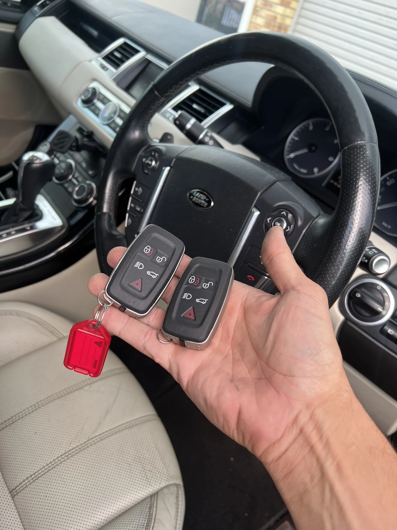 Person holding two Land Rover key fobs inside a vehicle with beige interior, showing the dashboard and steering wheel.