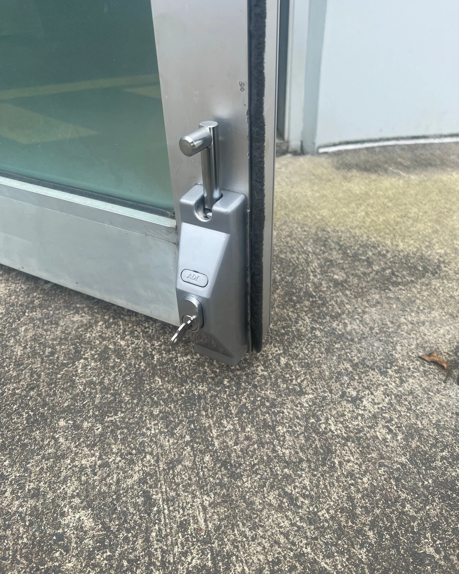 Close-up of a door with a security lock on the bottom corner, showing the door partially open on a concrete ground.