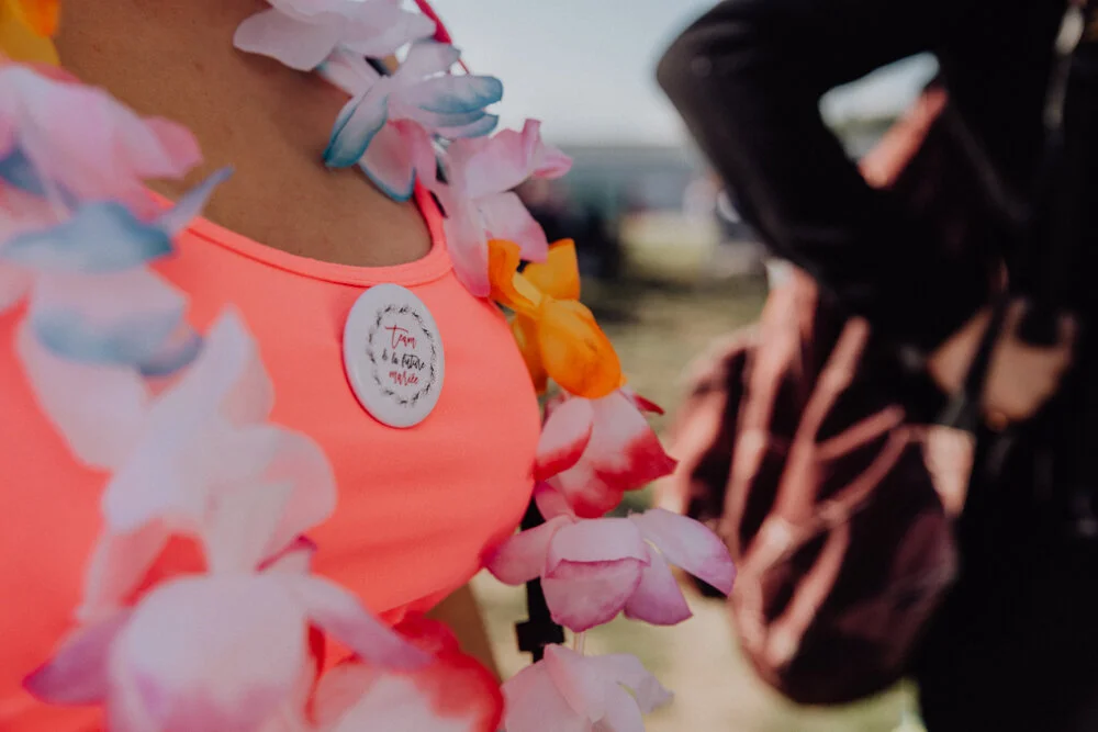 Une personne portant un collier de fleurs et un badge, rencontrant une autre personne vêtue de noir, probablement lors d'un événement en plein air.