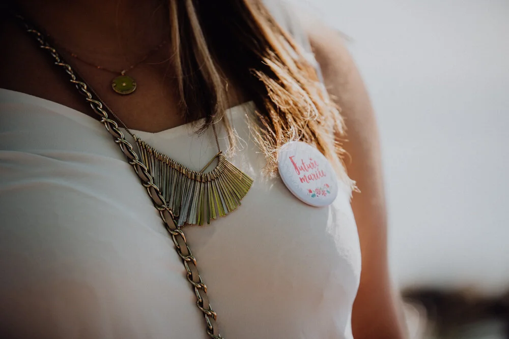 Une femme porte un collier en or, une chaîne en métal, et une broche avec écrit 'Féminité Marie'.