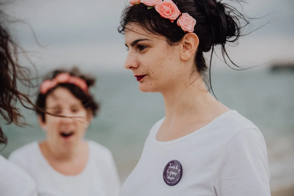 Deux femmes portant des fleurs roses dans les cheveux, debout près de la mer.