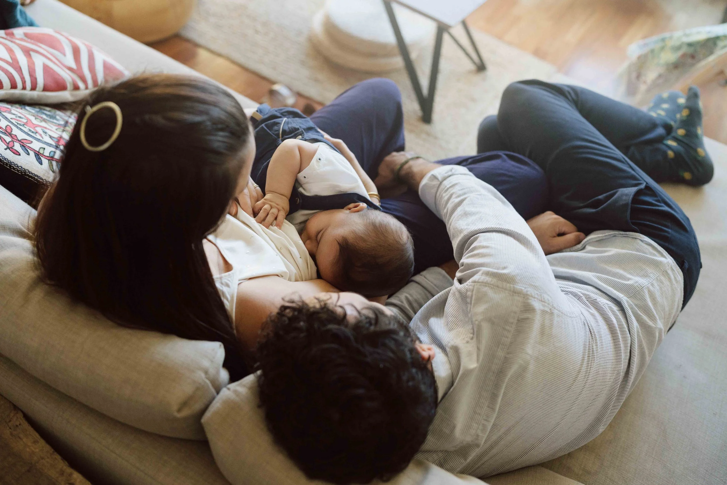 Jeune famille réunie sur le canapé autour de bébé pendant une séance maternité à domicile en Suisse romande