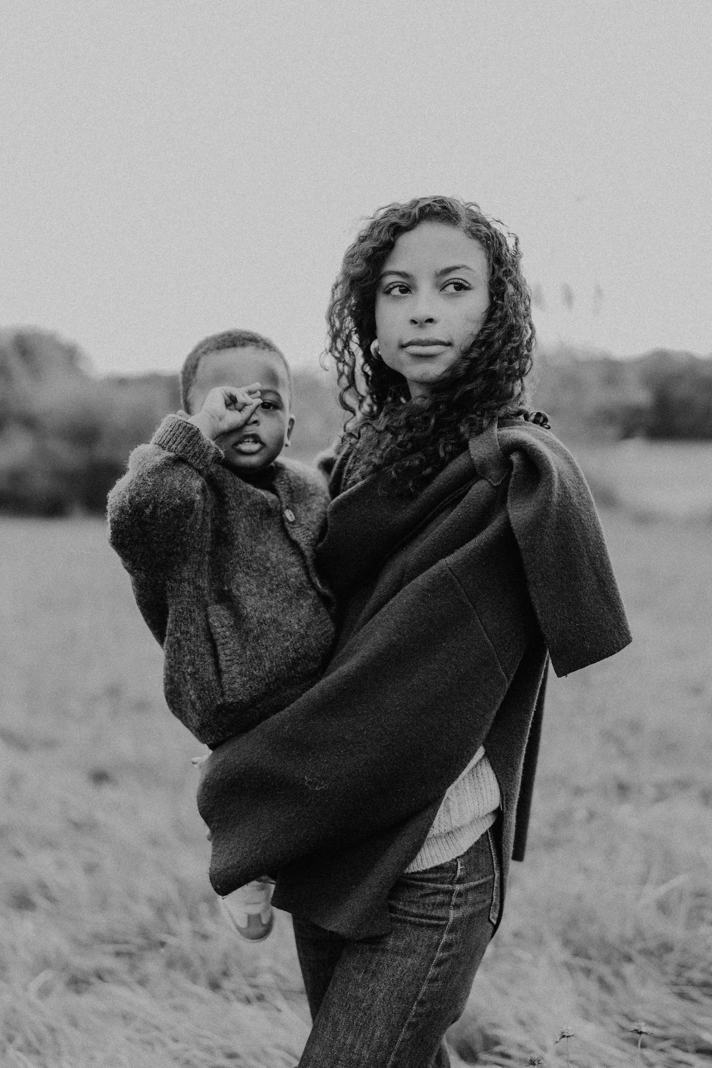Portrait noir et blanc d’une mère portant son enfant en pleine nature, une image lifestyle élégante et intemporelle capturée en extérieur par Nonante Émotions.