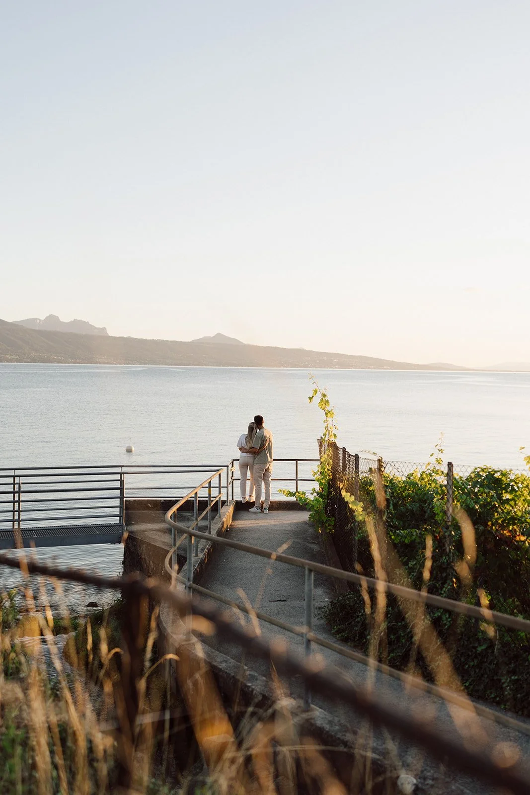 Vue poétique d’un couple enlacé au bord du Léman au coucher du soleil : une scène intime et lumineuse capturée entre calme, amour et horizon infini.