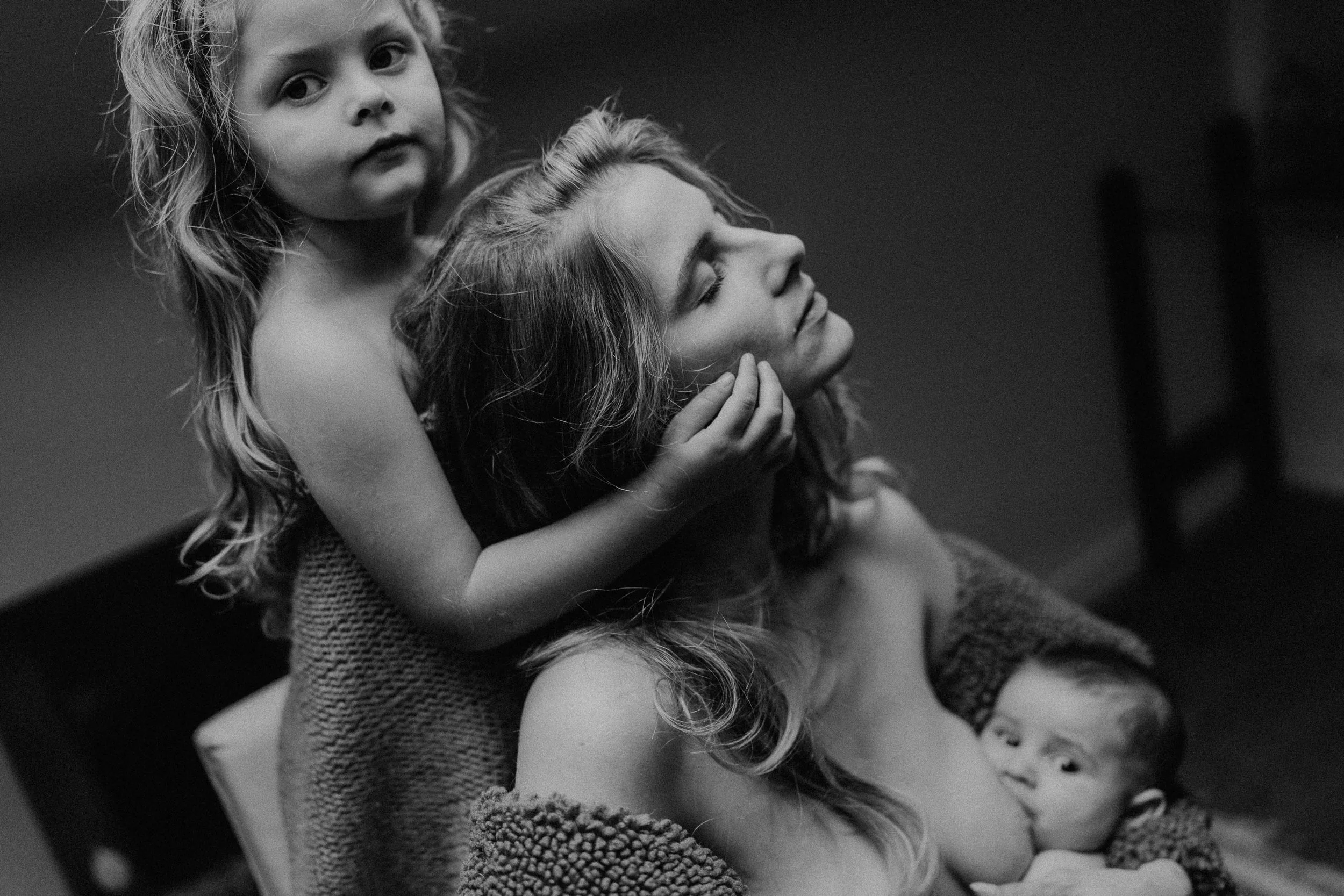 Portrait noir et blanc d’une mère avec ses deux enfants, entre tendresse, allaitement et complicité familiale, capturé dans un style intime et intemporel par Nonante Émotions.