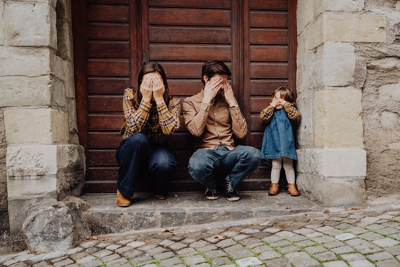Séance photo famille lifestyle en ville en Suisse : un moment ludique et spontané où parents et enfant jouent à cache-cache, capturé avec naturel et authenticité par Nonante Émotions.