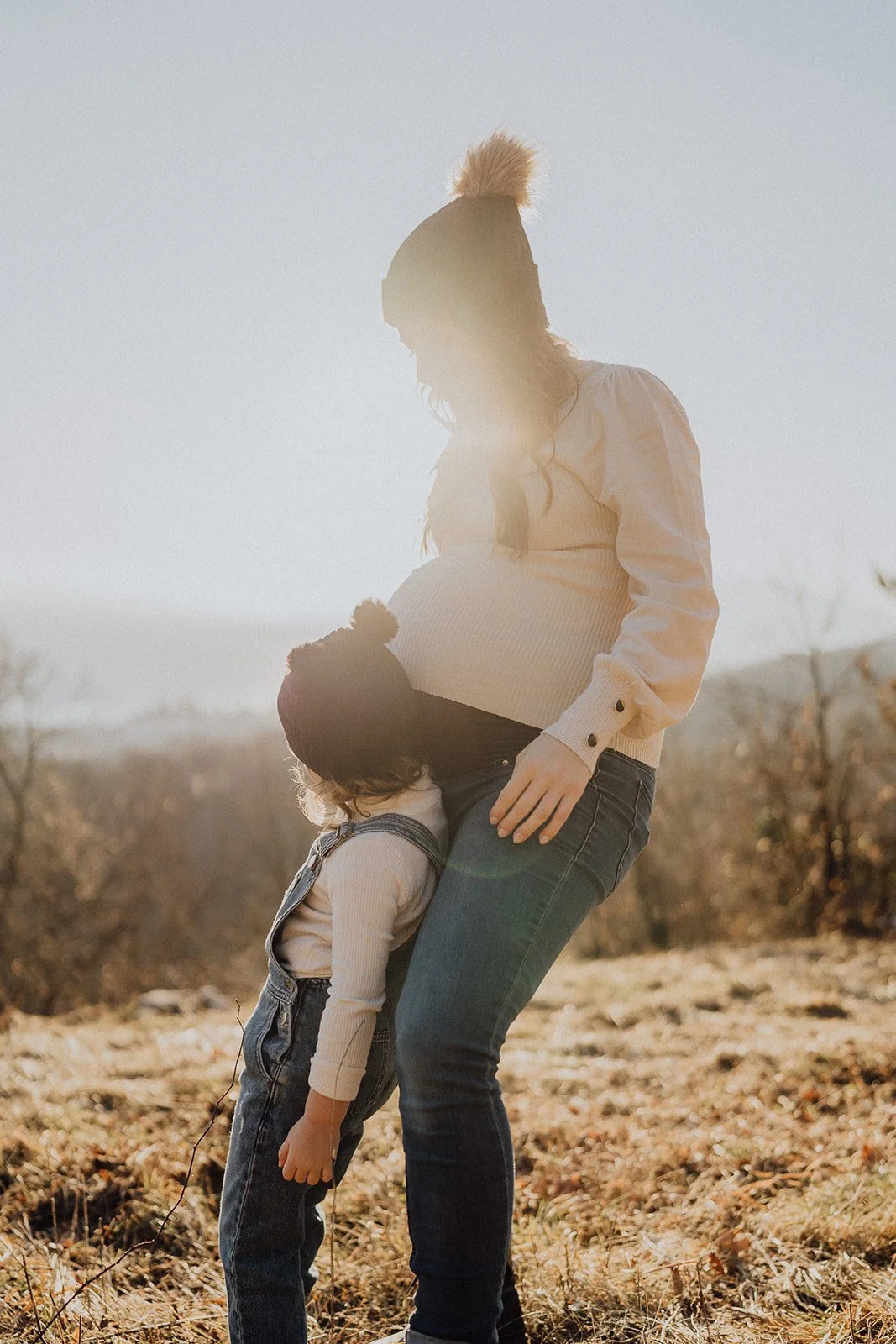Séance photo grossesse en extérieur en Suisse : un moment tendre entre une future maman et son enfant, baigné de lumière naturelle, capturé dans un style lifestyle doux et authentique par Nonante Émotions.