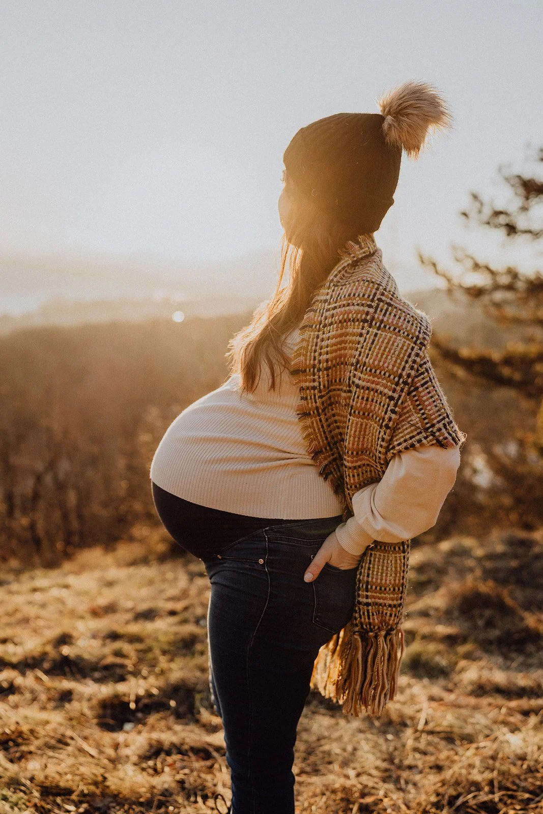 Portrait de grossesse en hiver baigné de lumière dorée : une future maman contemple l’horizon lors d’une séance maternité naturelle en extérieur.