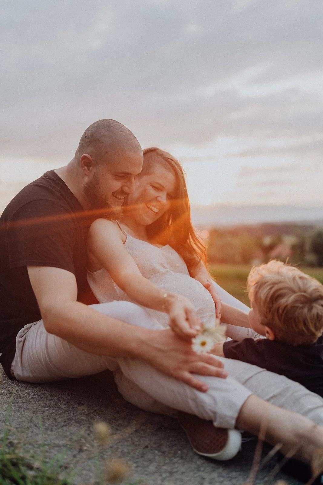 Séance maternité en famille au coucher du soleil : un couple et leur enfant partagent un moment tendre avant l’arrivée de bébé, capturé en lumière naturelle.